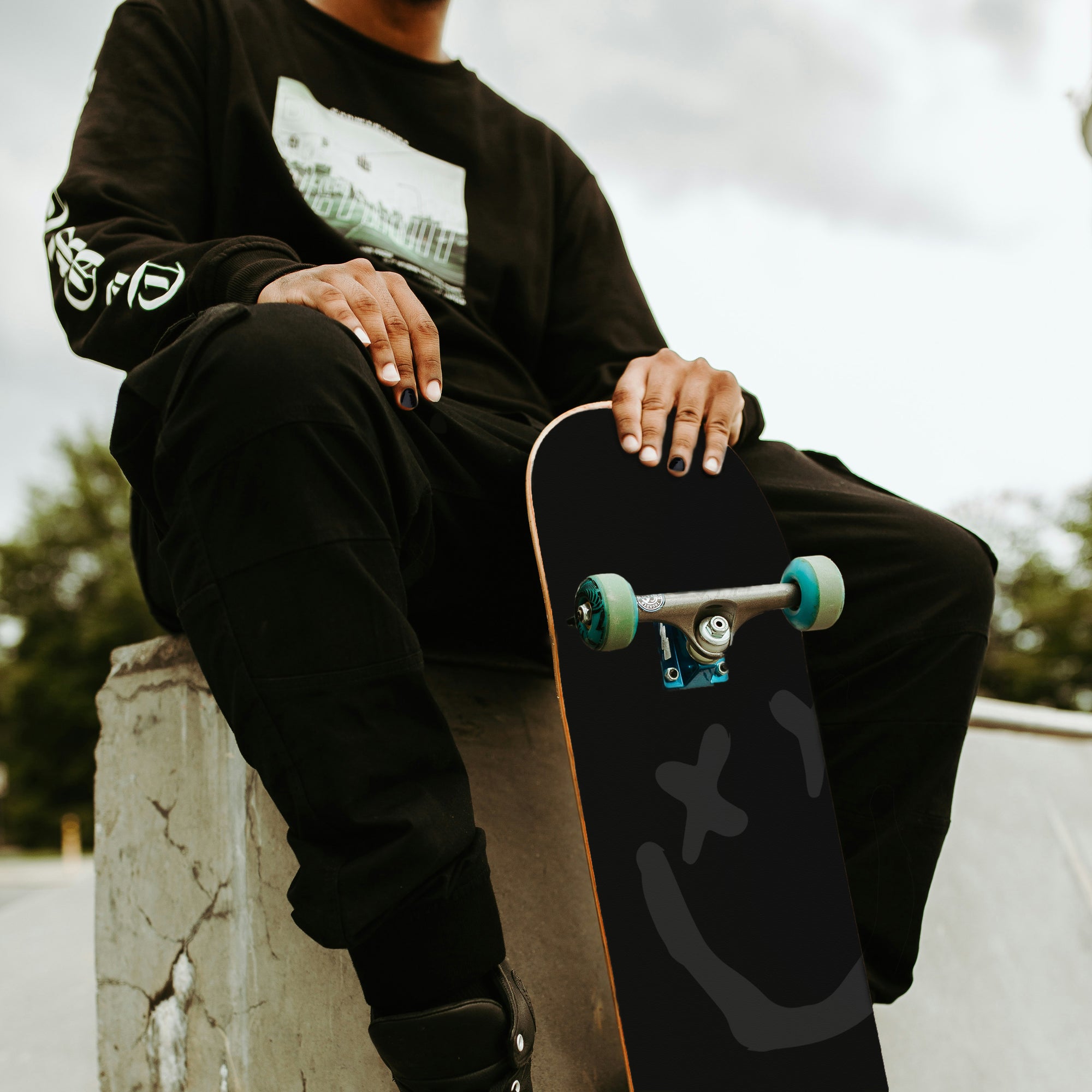 Man sitting and holding XY skateboard wearing Arcane X nail polish.