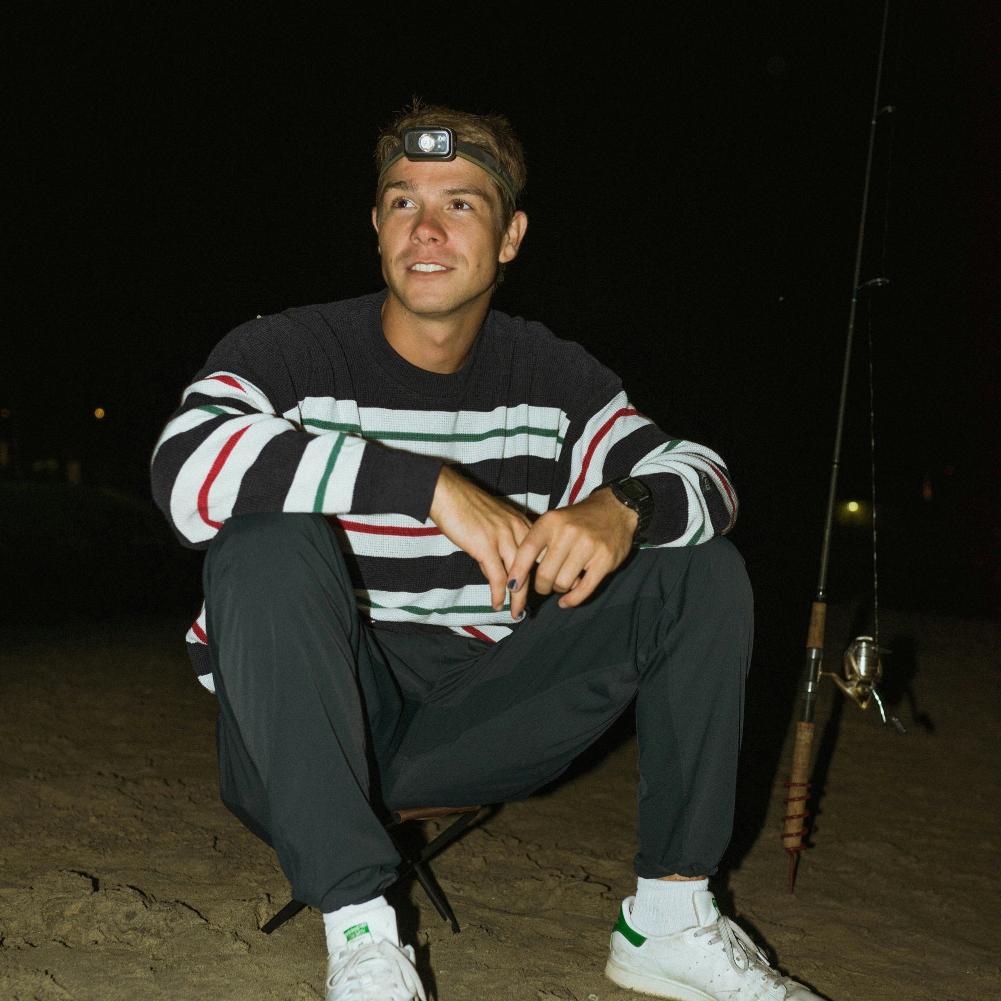 Man sitting on the sand with his fishing rod while wearing Arcane Y nail polish.