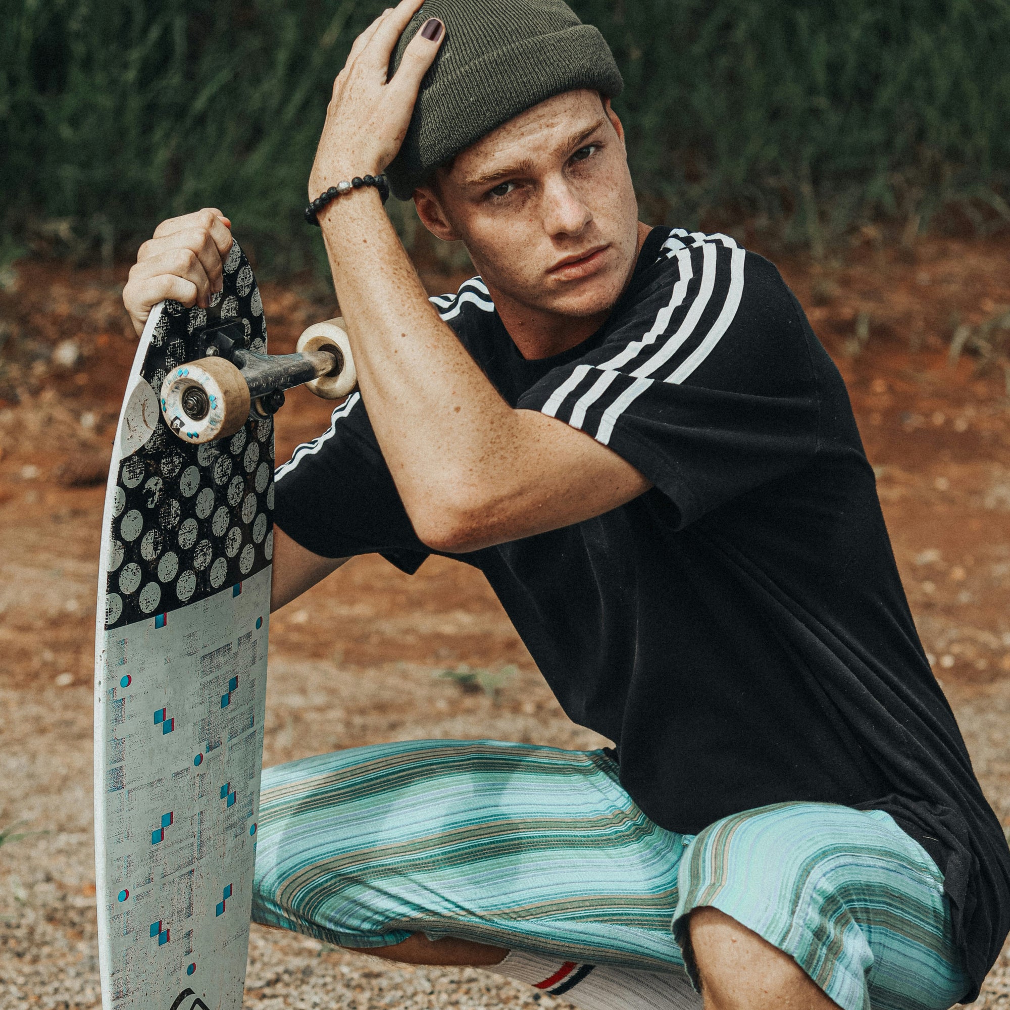 Man holding a skateboard and wearing the Rooted Duo.